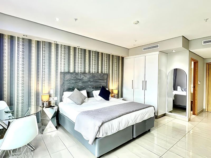 A well-maintained bedroom featuring built-in wardrobes, ducted air conditioning, recessed lighting, and modern tiled flooring with a decorative feature wall.