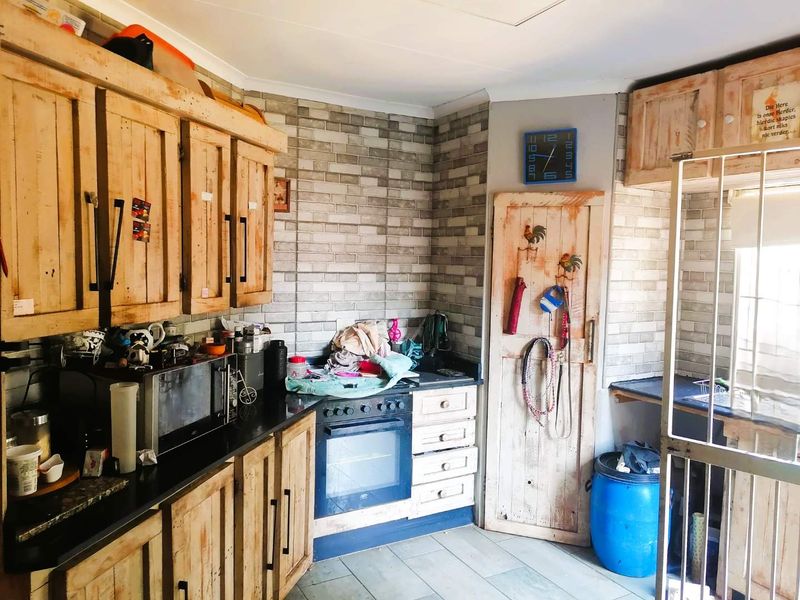A rustic-style kitchen featuring wooden cabinetry, black countertops, built-in oven, and brick-patterned wall tiles, offering a functional layout with potential for cosmetic updates.