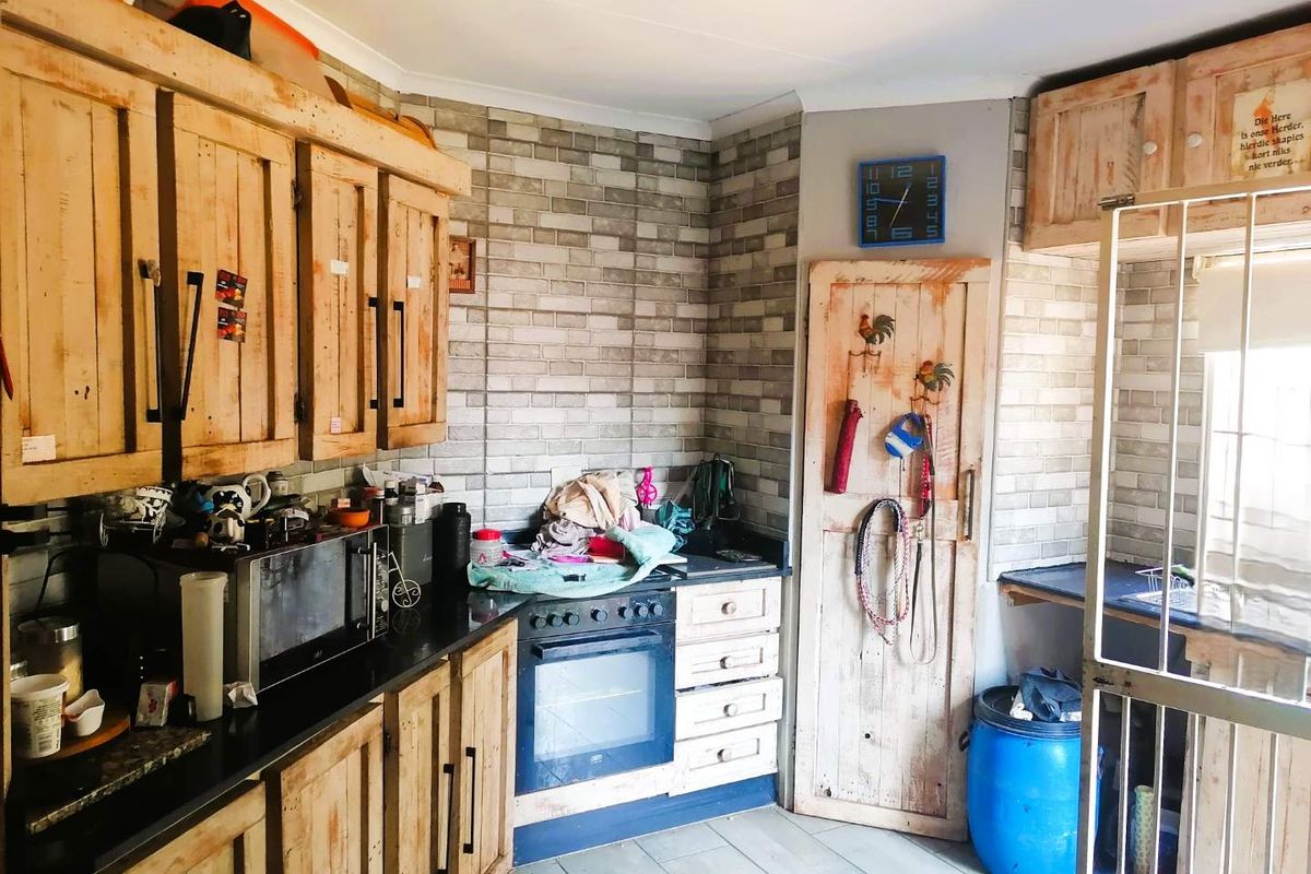 A rustic-style kitchen featuring wooden cabinetry, black countertops, built-in oven, and brick-patterned wall tiles, offering a functional layout with potential for cosmetic updates.