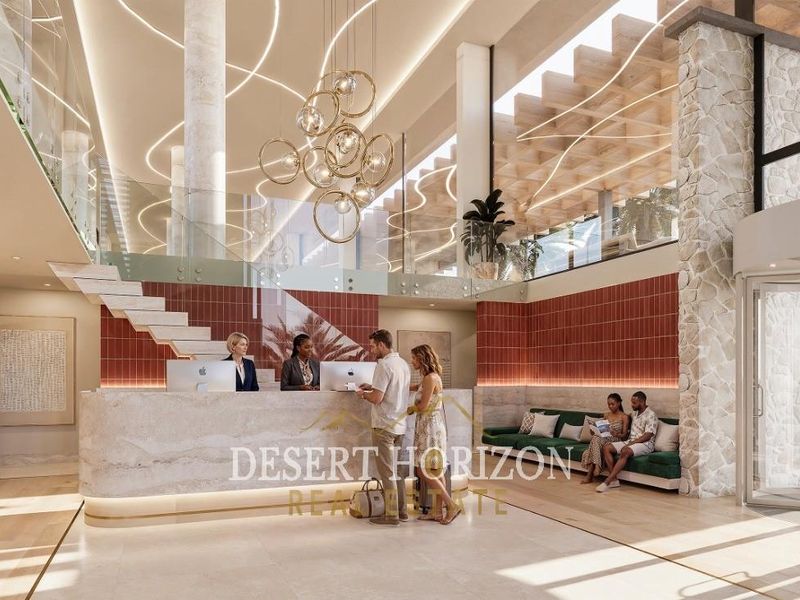 Modern hotel lobby featuring a stone reception desk, grand staircase with glass balustrade, and elegant architectural lighting in a spacious, high-ceilinged entrance area.