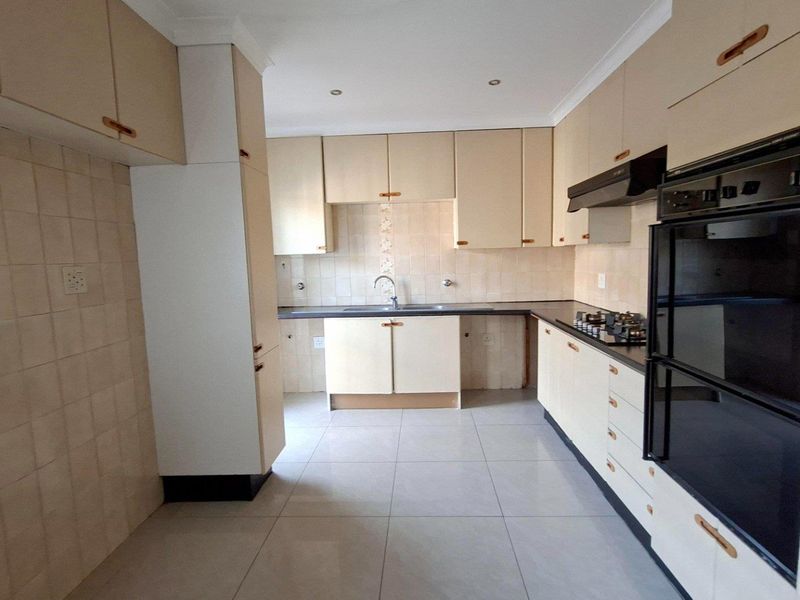 A functional kitchen featuring built-in cabinetry, tiled backsplash, integrated oven, hob, and extractor fan with neutral tiled flooring.
