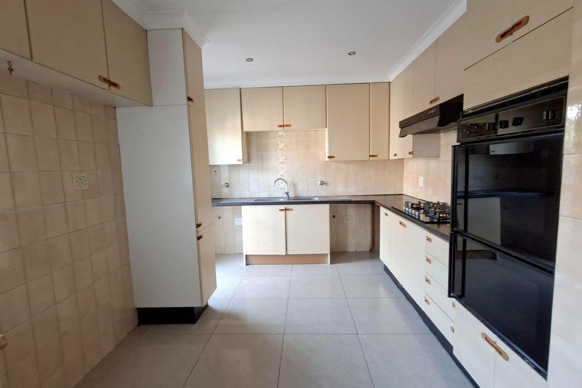 A functional kitchen featuring built-in cabinetry, tiled backsplash, integrated oven, hob, and extractor fan with neutral tiled flooring.