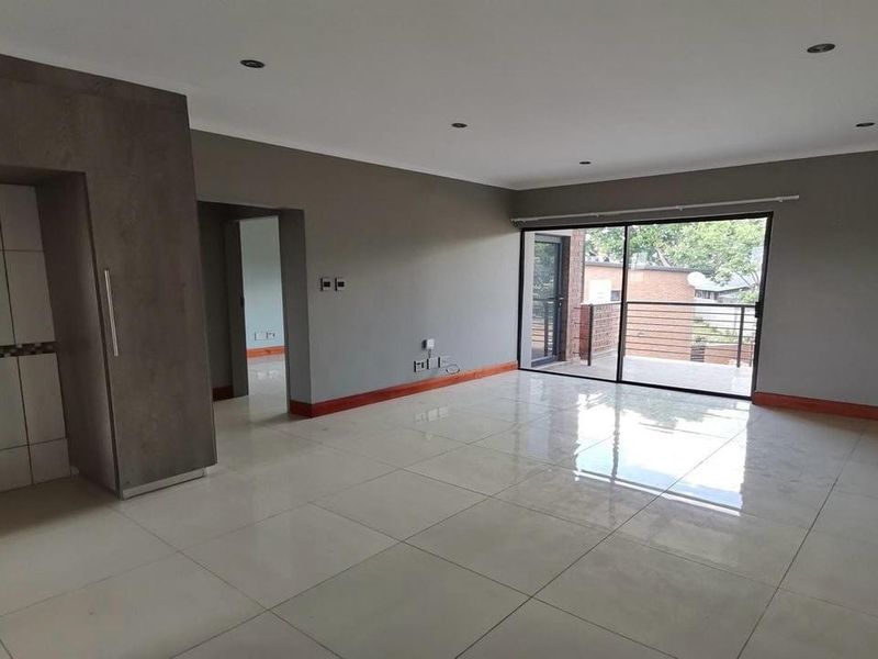 Spacious open-plan living area featuring neutral tiled flooring, recessed lighting, and large sliding glass doors leading to a private balcony.