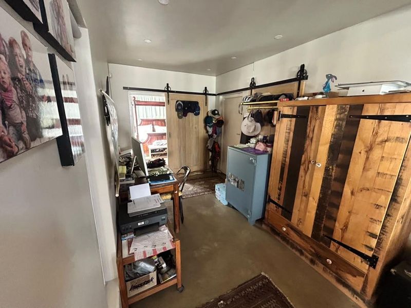 A functional home office space featuring concrete flooring, recessed lighting, and sliding barn-style doors providing access to adjacent areas.