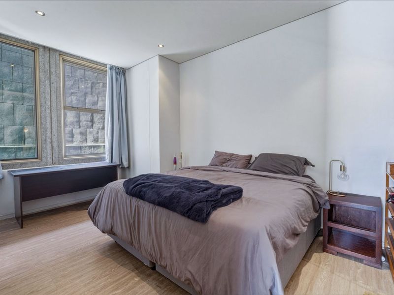 A well-lit bedroom featuring laminate flooring, recessed downlighting, and a built-in window ledge, offering a clean and functional living space.