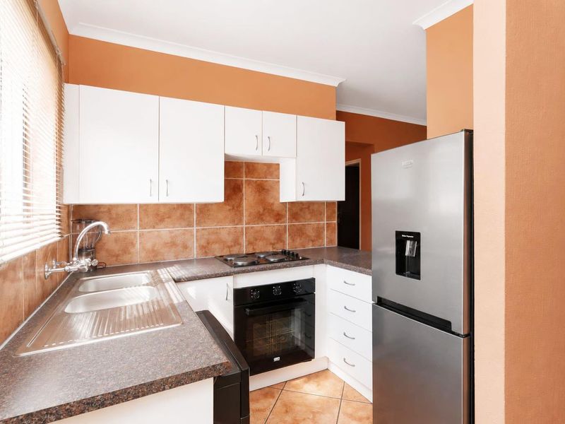 A functional kitchen featuring white cabinetry, dark laminate countertops, a built-in oven with gas hob, and tiled finishes throughout.