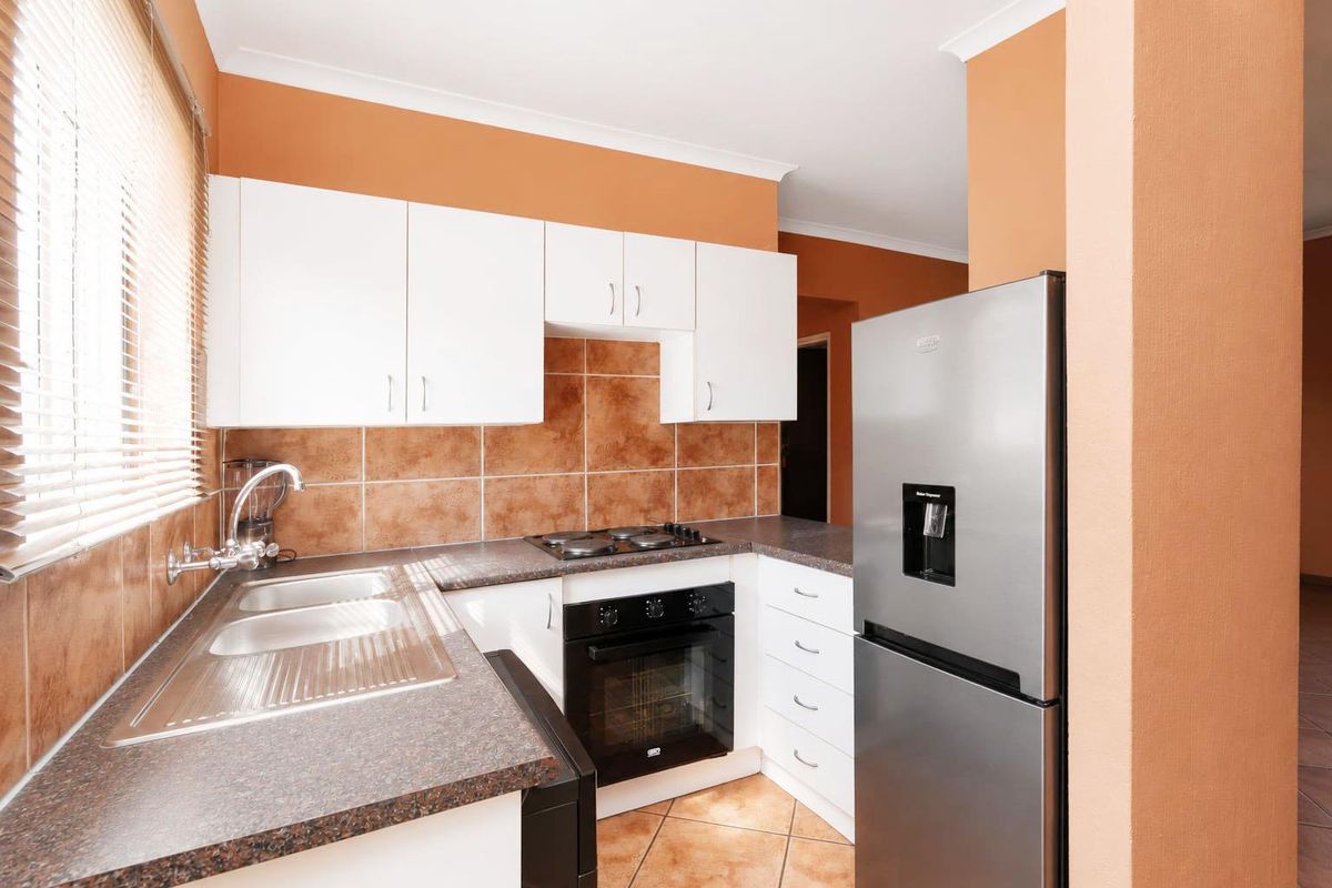A functional kitchen featuring white cabinetry, dark laminate countertops, a built-in oven with gas hob, and tiled finishes throughout.