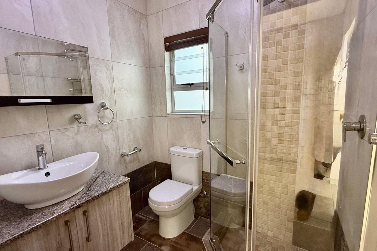 Modern bathroom featuring a glass-enclosed shower, vessel sink vanity with stone countertop, and neutral wall tiling.
