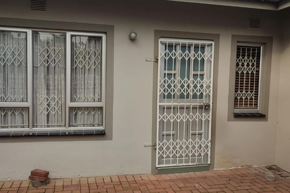 Rear exterior view featuring brick paving, security gates on doors and windows, and a tiled roof.