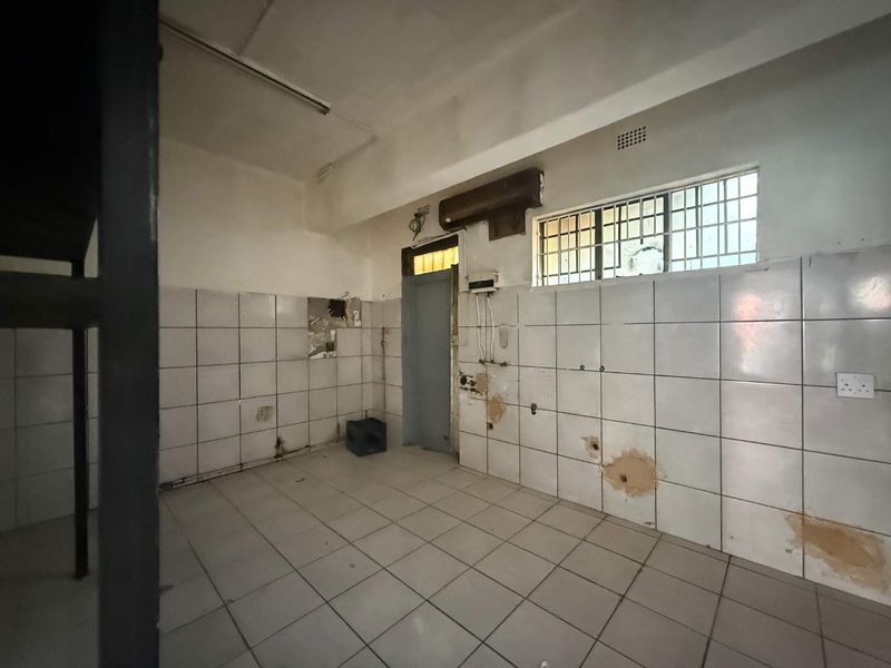 An empty, dated kitchen space featuring tiled walls and flooring, requiring renovation and repair to the wall finishes and electrical fixtures.