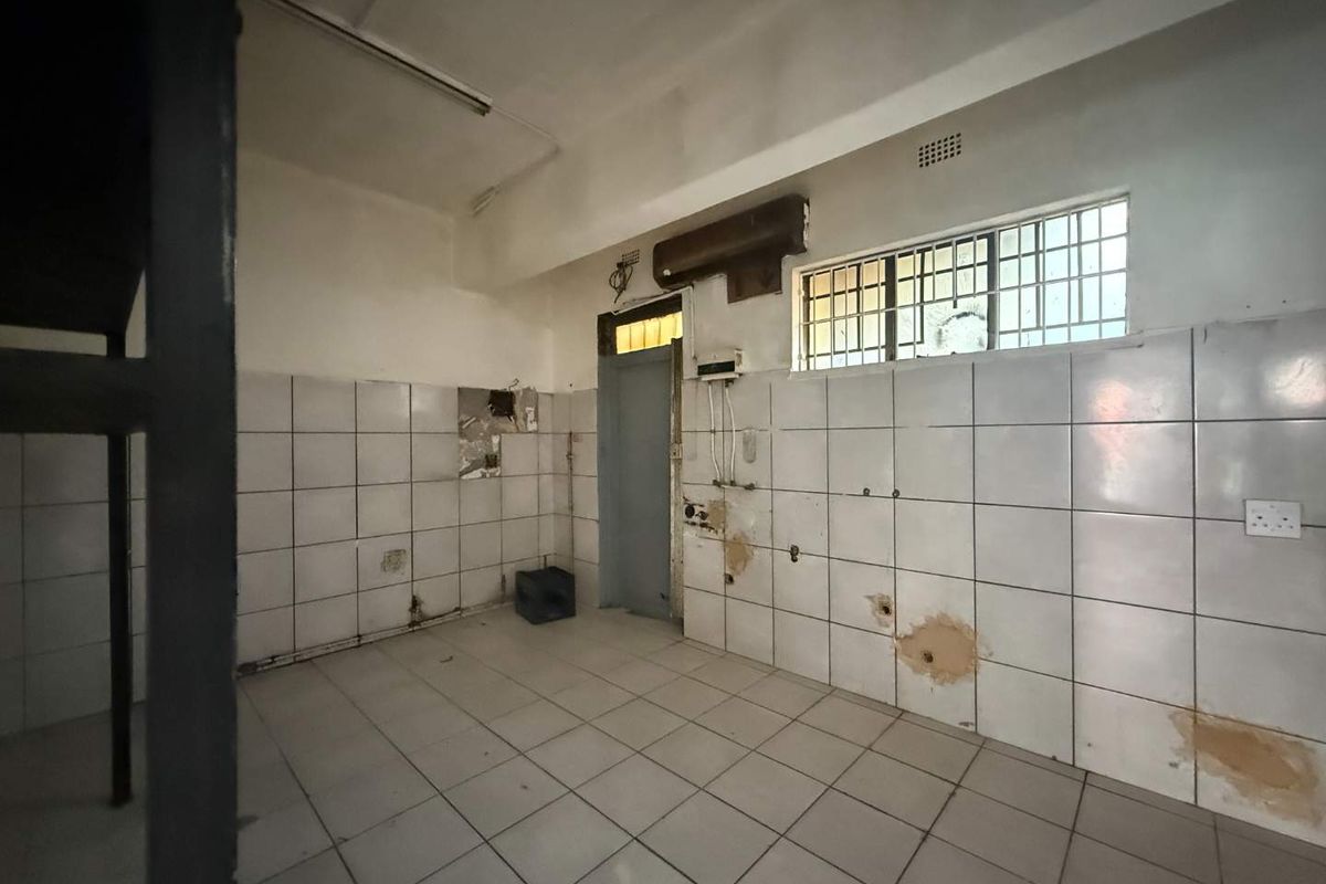 An empty, dated kitchen space featuring tiled walls and flooring, requiring renovation and repair to the wall finishes and electrical fixtures.