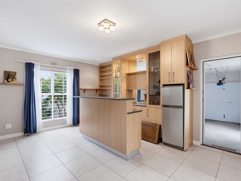 A functional bar area featuring built-in wooden cabinetry, a stone-topped counter, and tiled flooring, with direct access to an adjacent utility space.