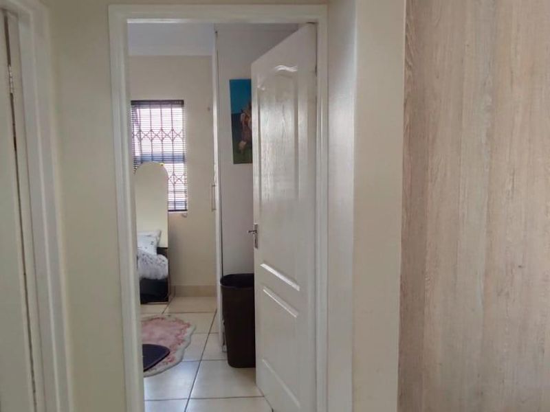 A view from the hallway looking into a bedroom and an adjacent kitchen area featuring built-in cabinetry and appliances.