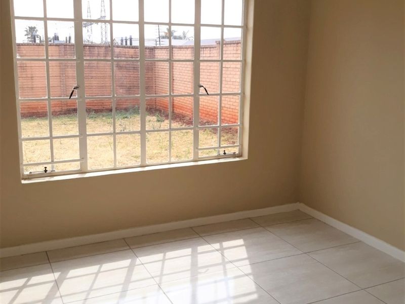 An empty bedroom featuring neutral tiled flooring and a large grid-pattern window overlooking the rear garden area.
