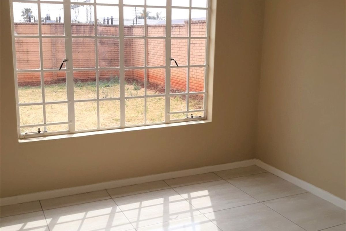 An empty bedroom featuring neutral tiled flooring and a large grid-pattern window overlooking the rear garden area.