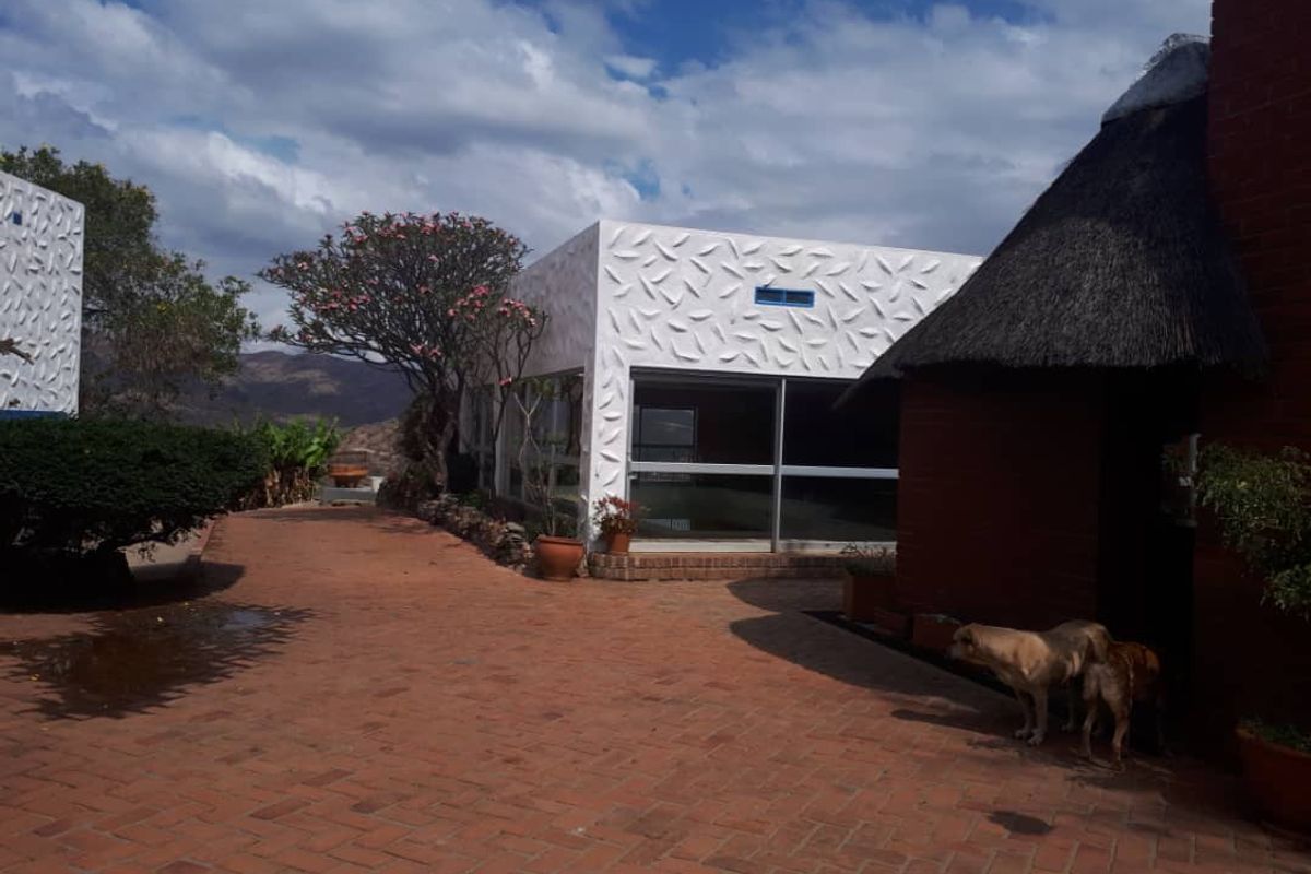 A view of the exterior courtyard featuring a modern white structure with textured walls alongside a traditional thatched-roof building and brick paved area.