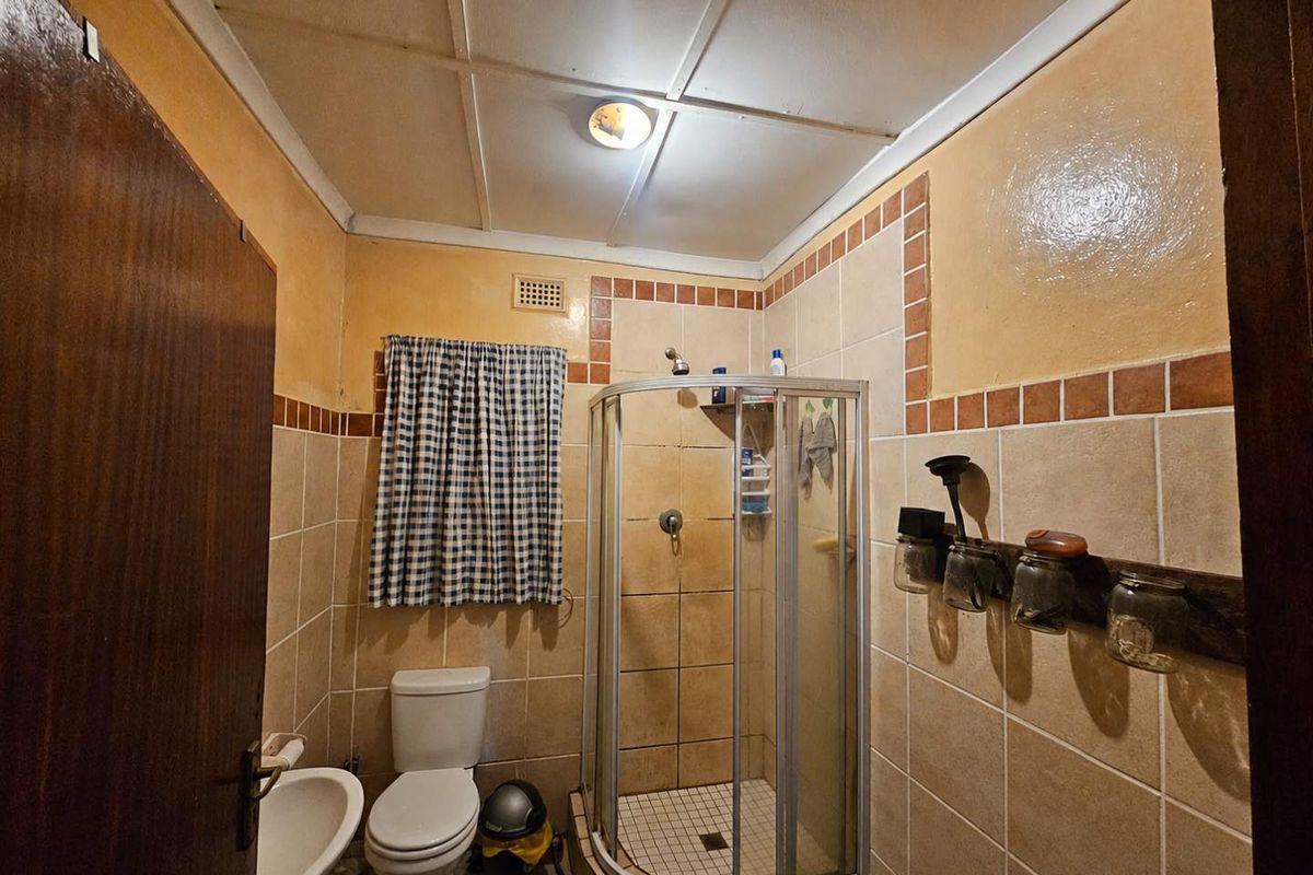 A compact bathroom featuring a corner shower enclosure, a standard toilet, and a wall-mounted basin with dated tile finishes and ceiling panels.