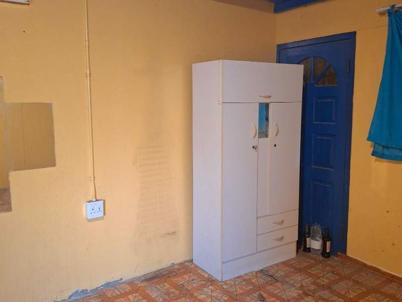 A bedroom featuring exposed blue ceiling beams, tiled flooring, and yellow walls, requiring cosmetic updates and repairs to the flooring and wall finishes.