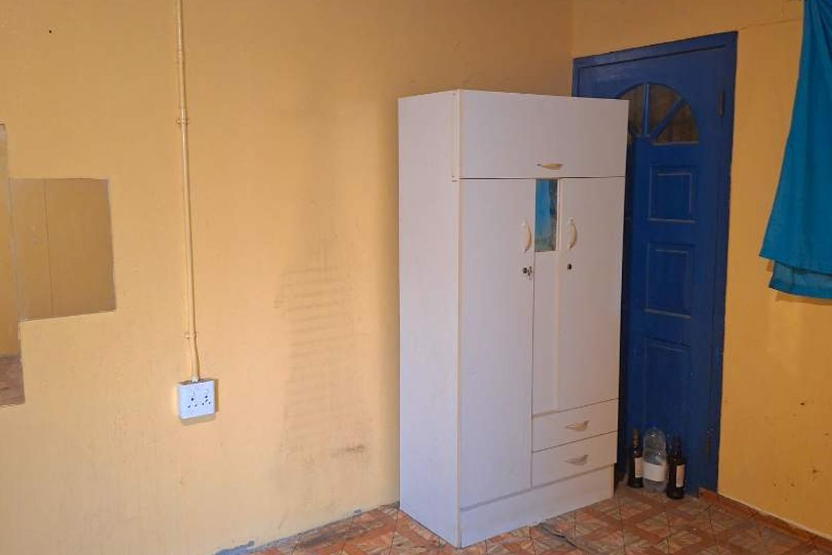 A bedroom featuring exposed blue ceiling beams, tiled flooring, and yellow walls, requiring cosmetic updates and repairs to the flooring and wall finishes.