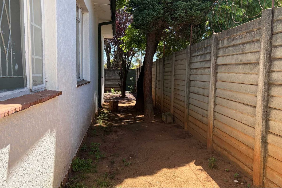 A narrow side passage of the property featuring a precast concrete boundary wall with security razor wire and basic window security bars.