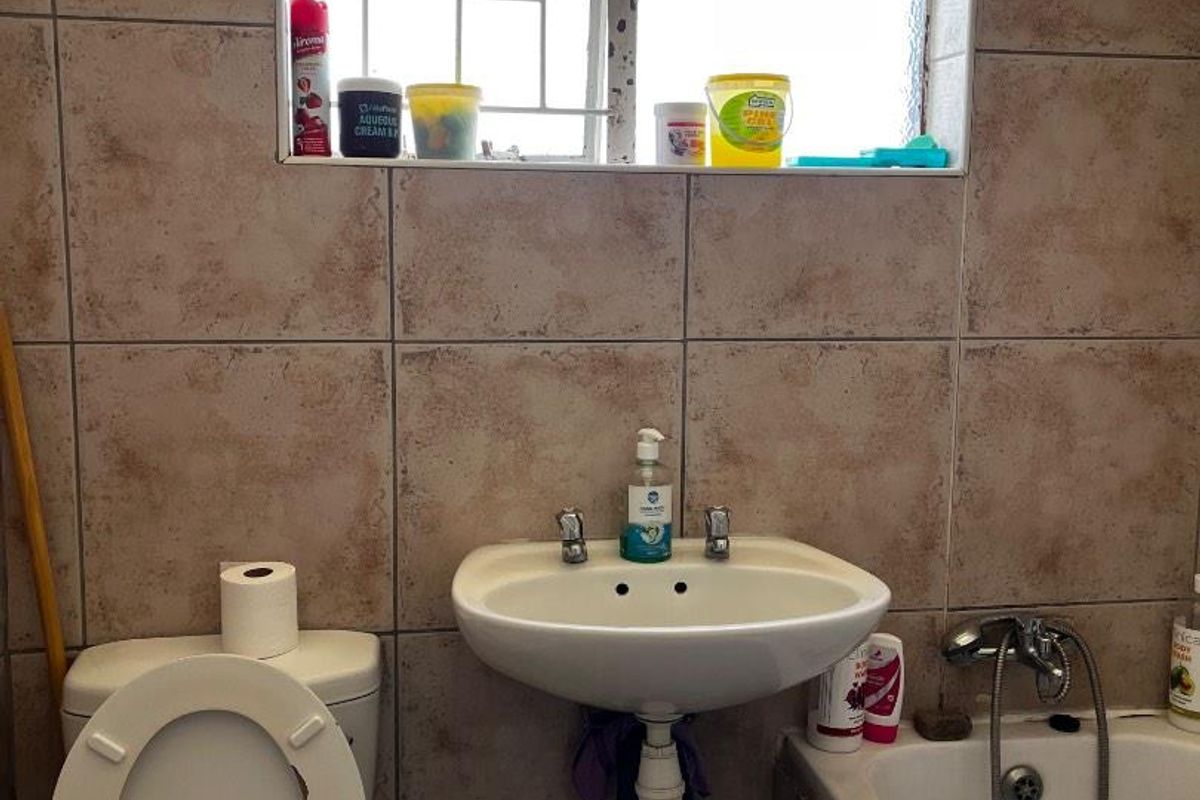 A compact bathroom featuring a wall-mounted basin, standard toilet, and a bathtub with a shower mixer, finished with dated ceramic wall tiles.