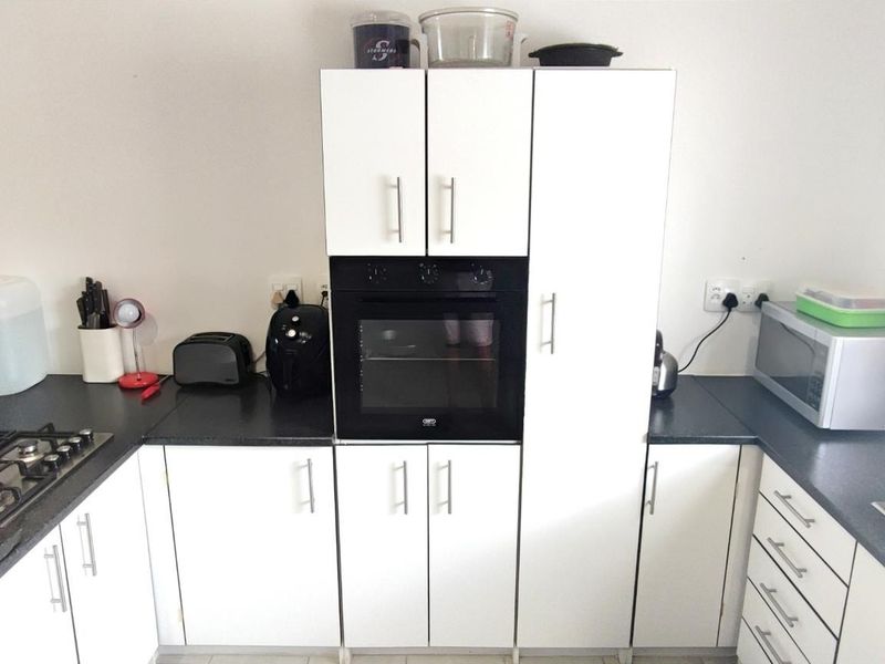 A functional kitchen featuring white cabinetry, dark laminate countertops, a built-in oven, and a gas hob with a tiled splashback.