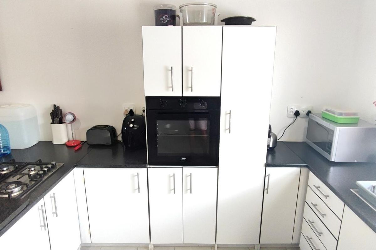 A functional kitchen featuring white cabinetry, dark laminate countertops, a built-in oven, and a gas hob with a tiled splashback.