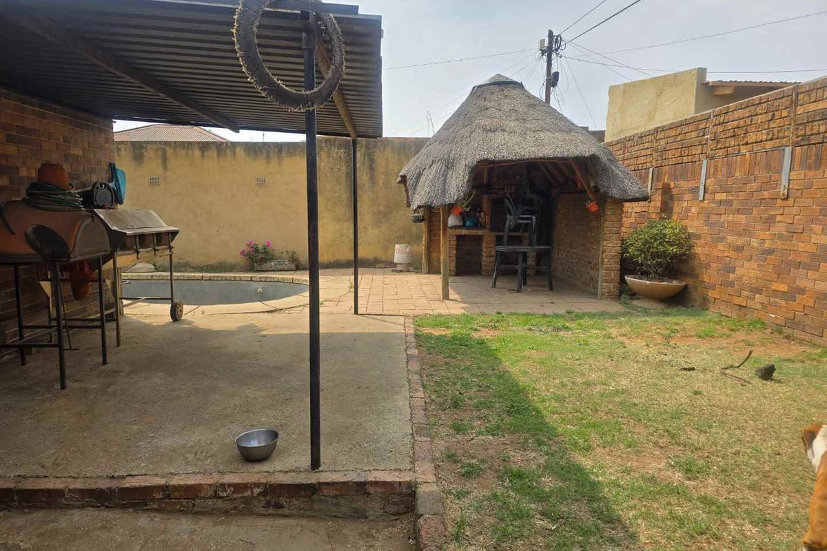 Outdoor entertainment area featuring a covered patio, a thatched lapa with built-in braai, a small swimming pool, and a brick-walled garden.