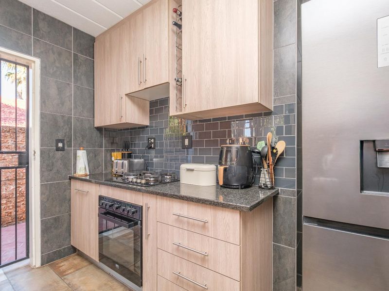 Modern kitchen featuring light wood cabinetry, granite countertops, a gas hob, built-in oven, and stylish dark tiled backsplash with direct access to an outdoor area.