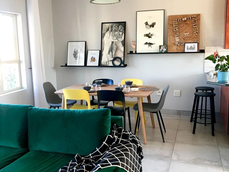 An open-plan living and dining area featuring neutral tiled flooring, modern pendant lighting, and floating wall shelves, creating a bright and functional living space.