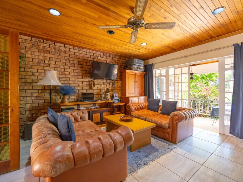 Cozy living room featuring an exposed brick wall, warm timber ceiling with downlights, and direct access to an outdoor patio through glass doors.
