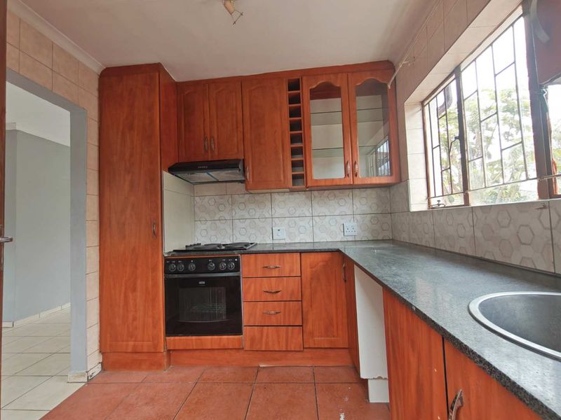 A dated kitchen featuring wooden cabinetry, granite countertops, a built-in oven with gas hob, and tiled finishes throughout.