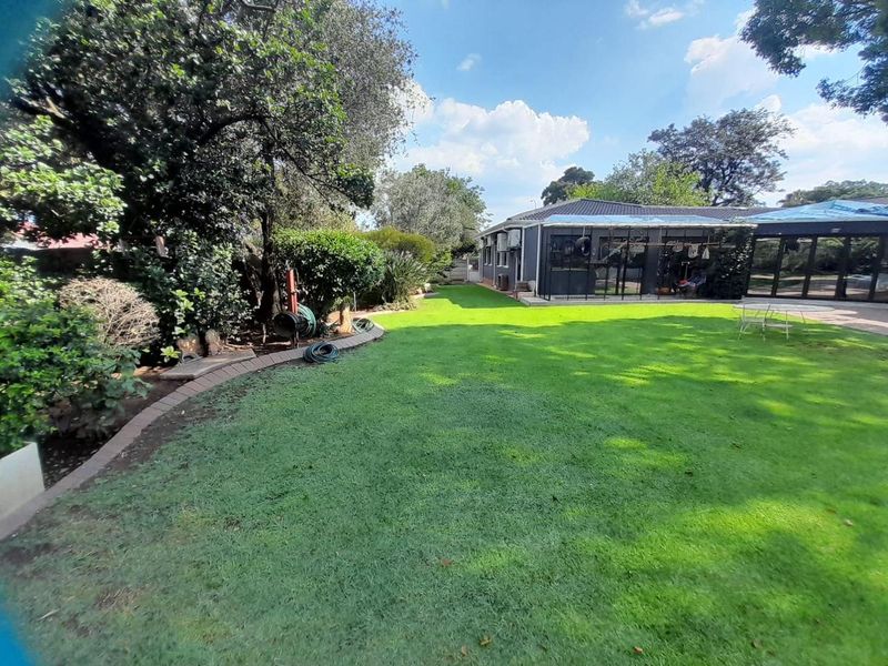 A spacious rear garden featuring a well-maintained lawn, paved garden borders, and a covered patio area attached to the main house structure.