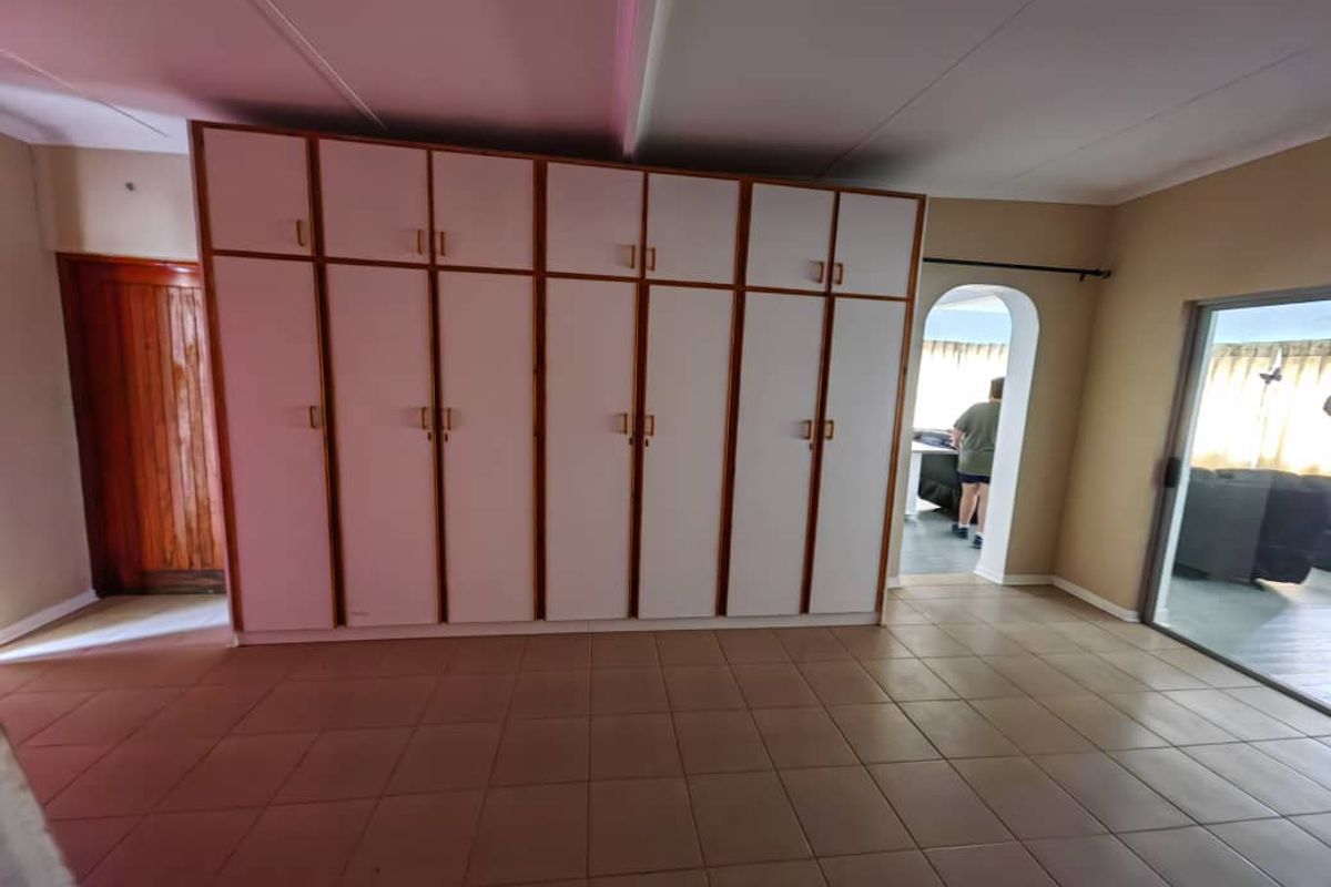 Spacious bedroom featuring extensive built-in cupboards, neutral tiled flooring, and direct access to an outdoor area through a sliding door.
