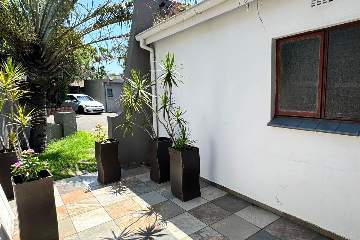 A paved rear patio area featuring an exterior wall with a window and visible roof guttering requiring maintenance.