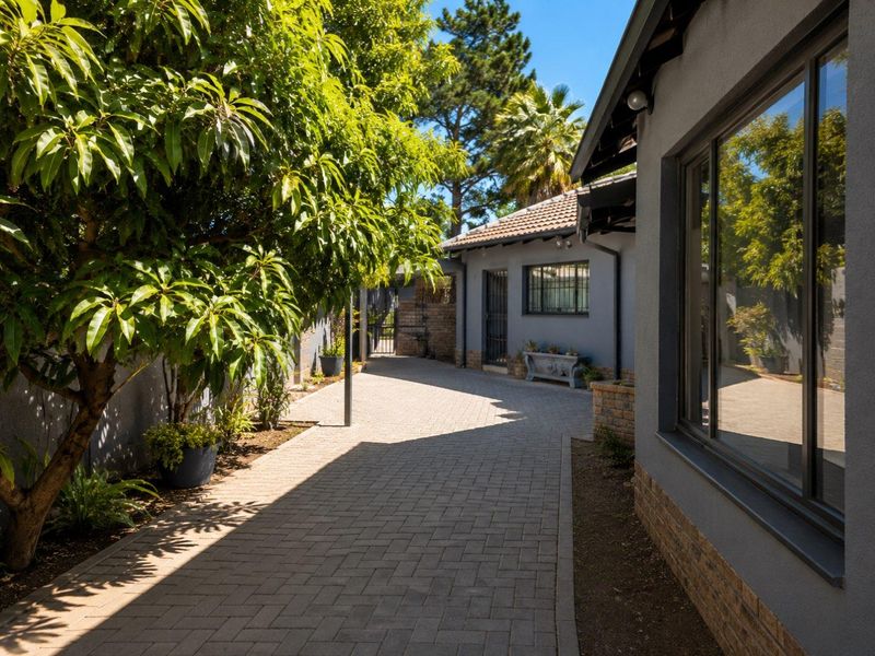 A well-maintained paved side pathway and driveway area featuring brick boundary walls, mature landscaping, and secure window bars.