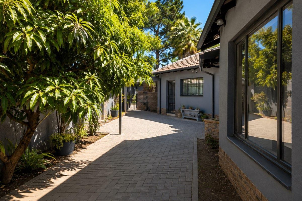 A well-maintained paved side pathway and driveway area featuring brick boundary walls, mature landscaping, and secure window bars.