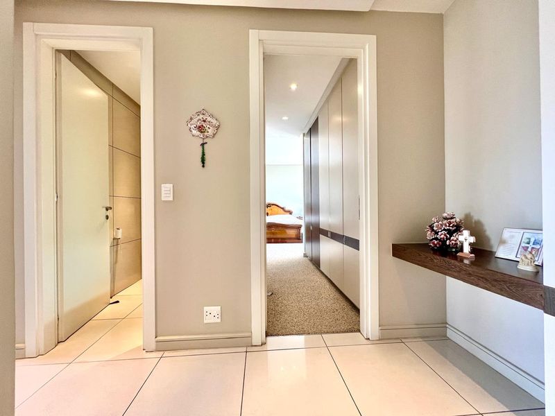 A well-maintained hallway featuring tiled flooring, recessed lighting, and built-in cupboards, providing access to adjacent rooms.