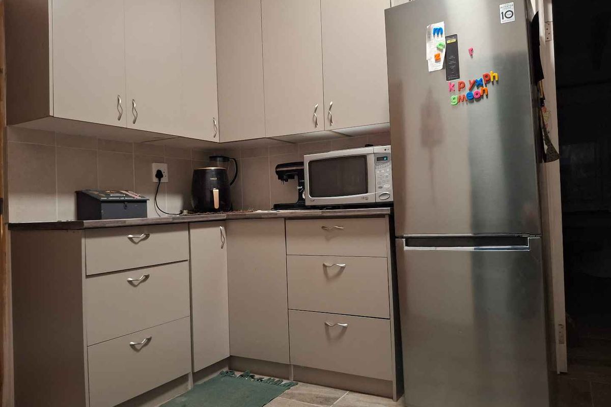 A compact kitchen featuring neutral-toned cabinetry, tiled splashbacks, and tiled flooring, providing a functional and organized food preparation area.