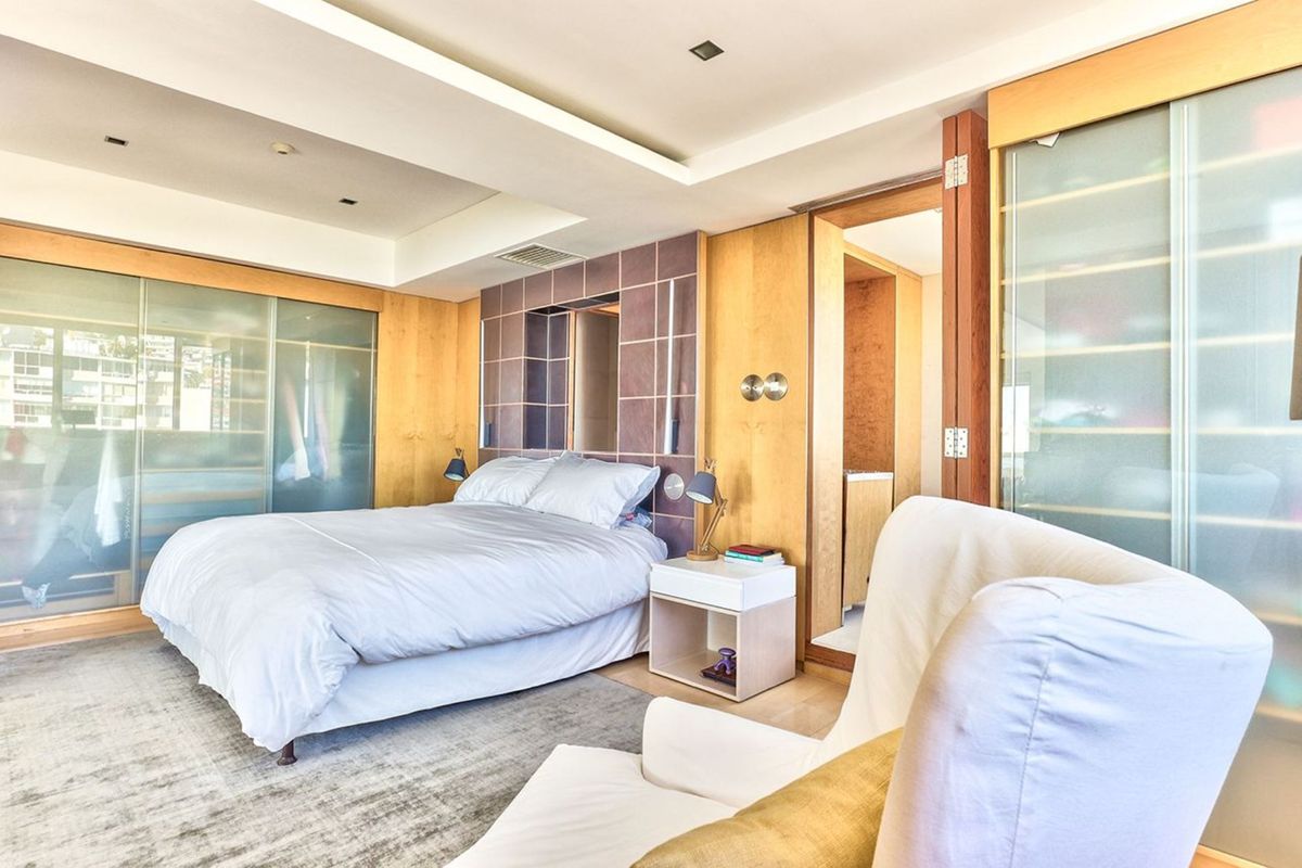 A well-appointed bedroom featuring extensive built-in wood cabinetry, a tiled feature wall, recessed ceiling lighting, and direct access to an en-suite bathroom.