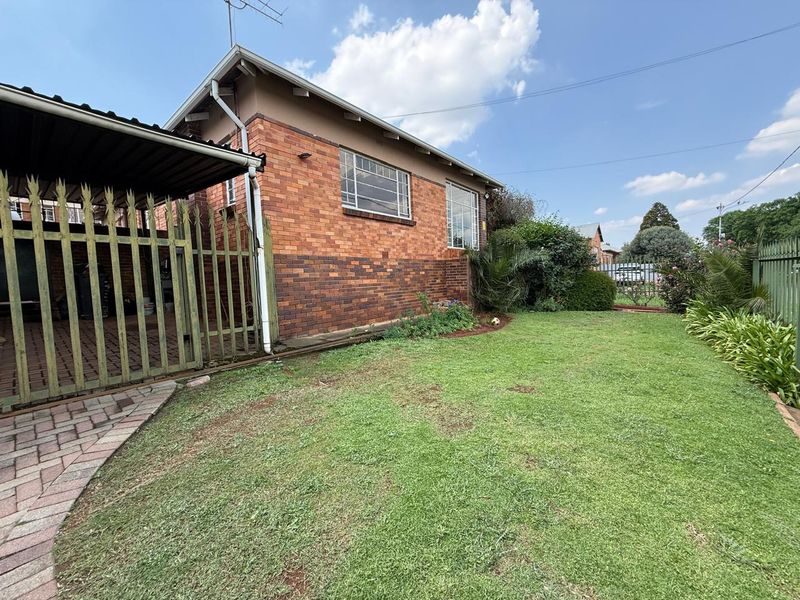 A view of the rear exterior featuring a brick facade, a covered carport, paved driveway, and a well-maintained lawn area.