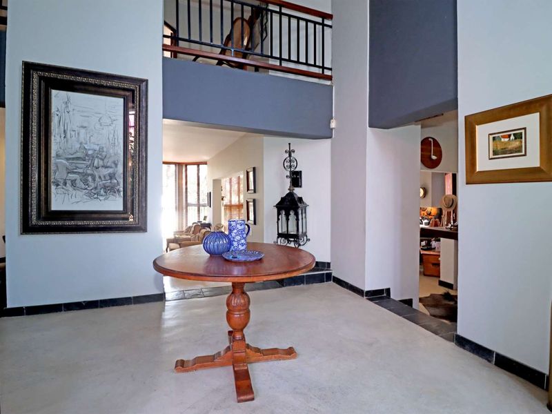 Spacious double-volume entrance hall featuring tiled flooring, a mezzanine level with a metal balustrade, and open access to adjoining living areas.