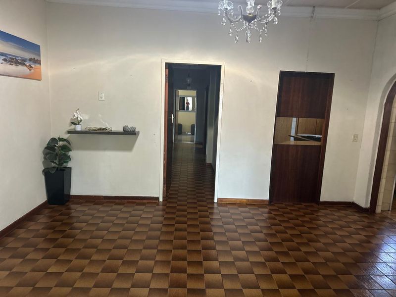 A spacious living area featuring classic parquet flooring, a decorative crystal chandelier, and a central hallway leading to the rest of the home.