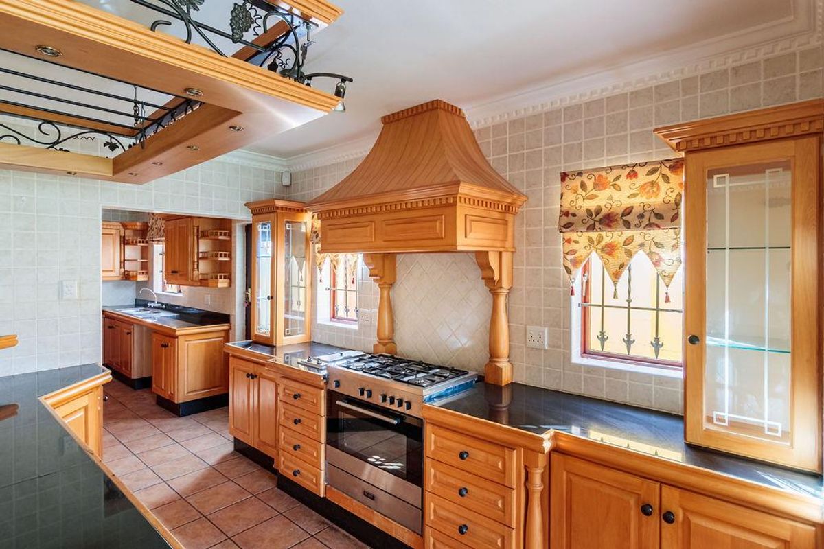 Traditional kitchen featuring solid wood cabinetry, granite countertops, a gas hob with a decorative extractor hood, and an adjoining scullery area.