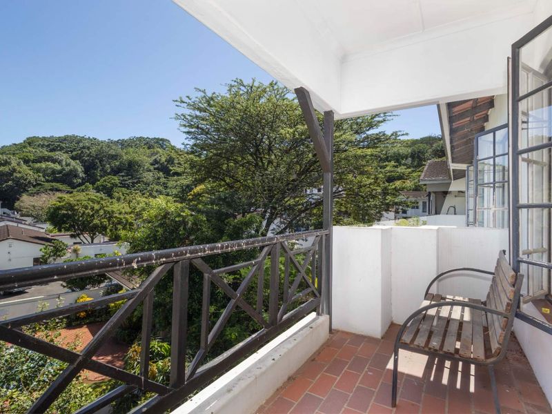 A covered balcony featuring terracotta tile flooring and a metal railing, offering pleasant views of the surrounding greenery and neighborhood.