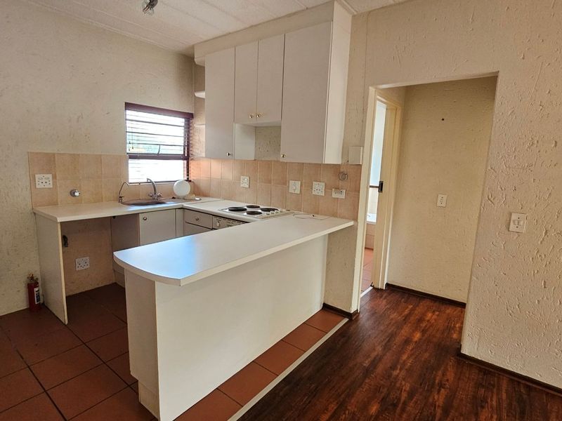 A functional kitchen featuring built-in cabinetry, a breakfast bar, electric hob, and a mix of tiled and laminate flooring.