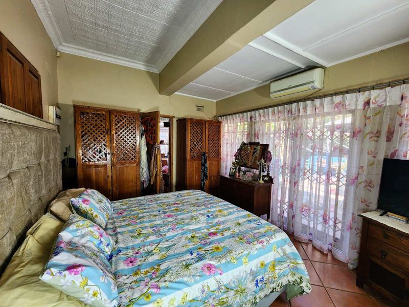 Spacious bedroom featuring built-in wooden cupboards, split-system air conditioning, tiled flooring, and direct access to the outdoor area through sliding glass doors.