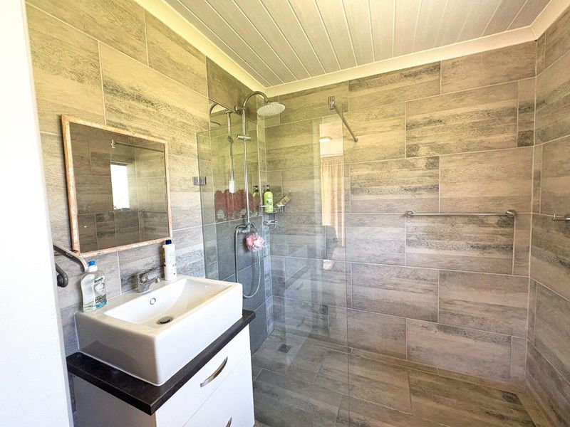 Modern bathroom featuring a spacious walk-in shower with glass screen, contemporary vessel sink vanity, and neutral wood-look wall and floor tiling.