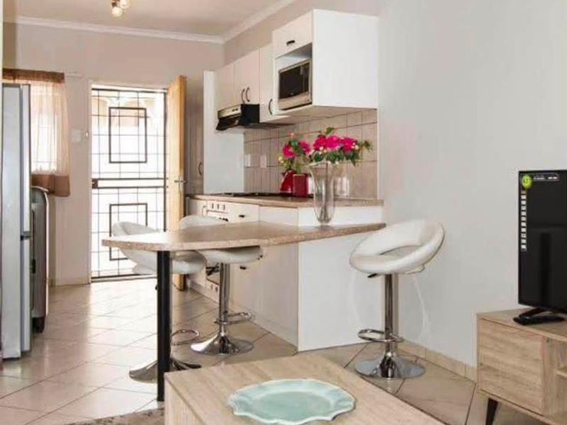 Open-plan living area featuring a compact kitchen with built-in cabinetry, laminate countertops, and tiled flooring, leading to a secure exterior entrance.