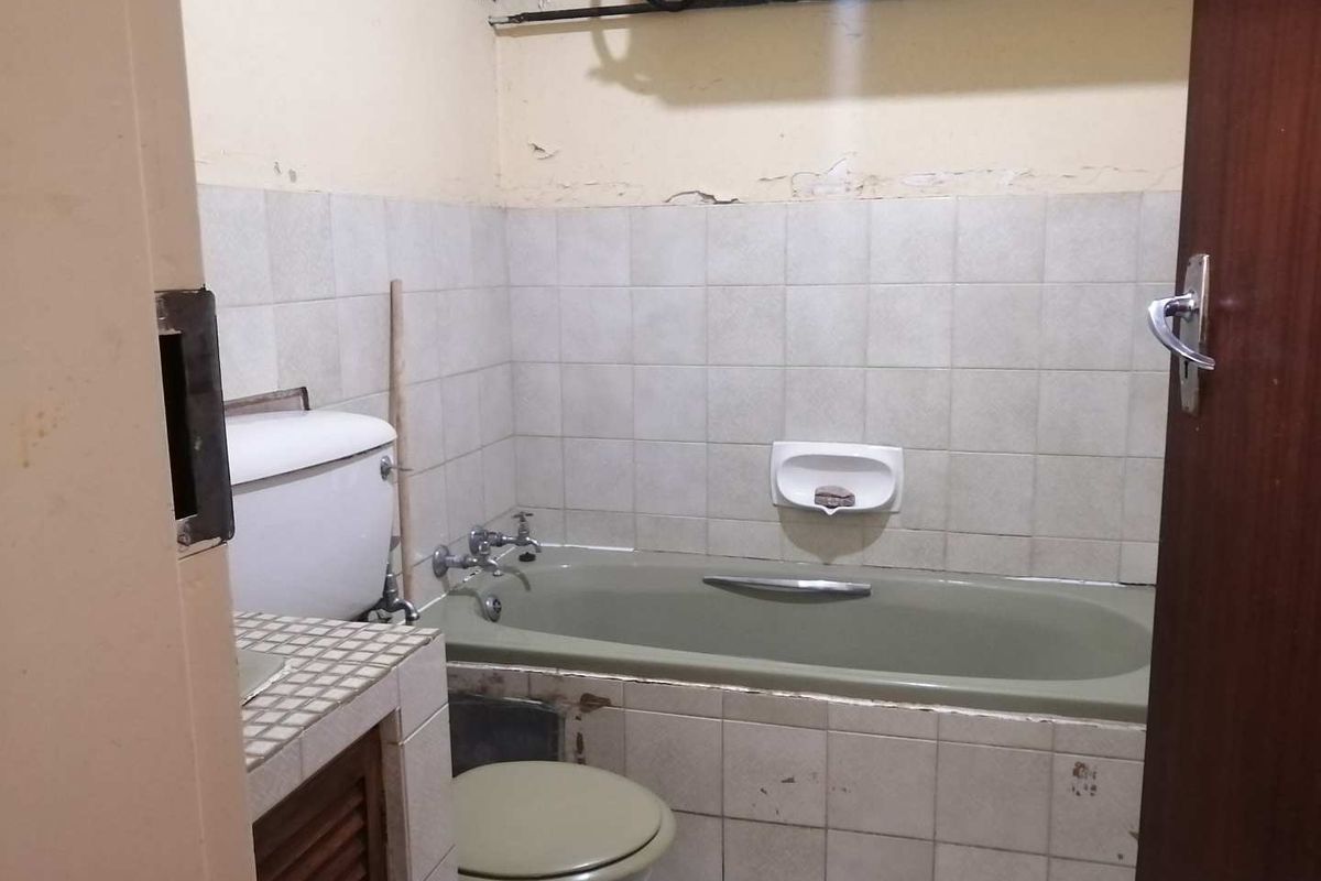 A dated bathroom featuring a built-in bathtub, toilet, and tiled vanity area, requiring cosmetic updates and maintenance to the wall finishes.